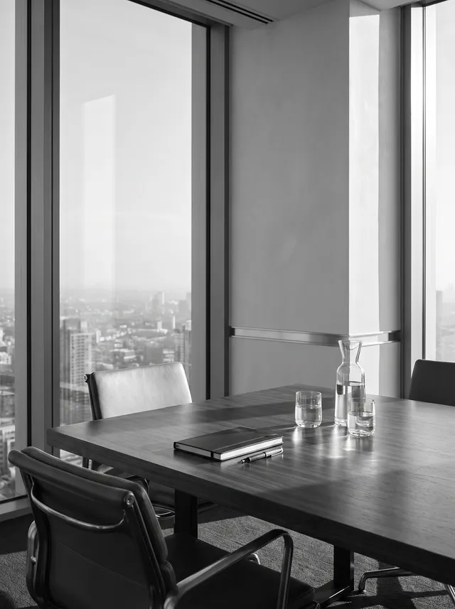 A private meeting room high in a modern office tower, a polished table set with a notebook and water, city skyline beyond the glass